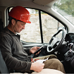 Lioton® Gel la locul de muncӑ, Bǎrbat purtând o cascӑ roșie, stând într-un camion de lucru, verificându-și telefonul.